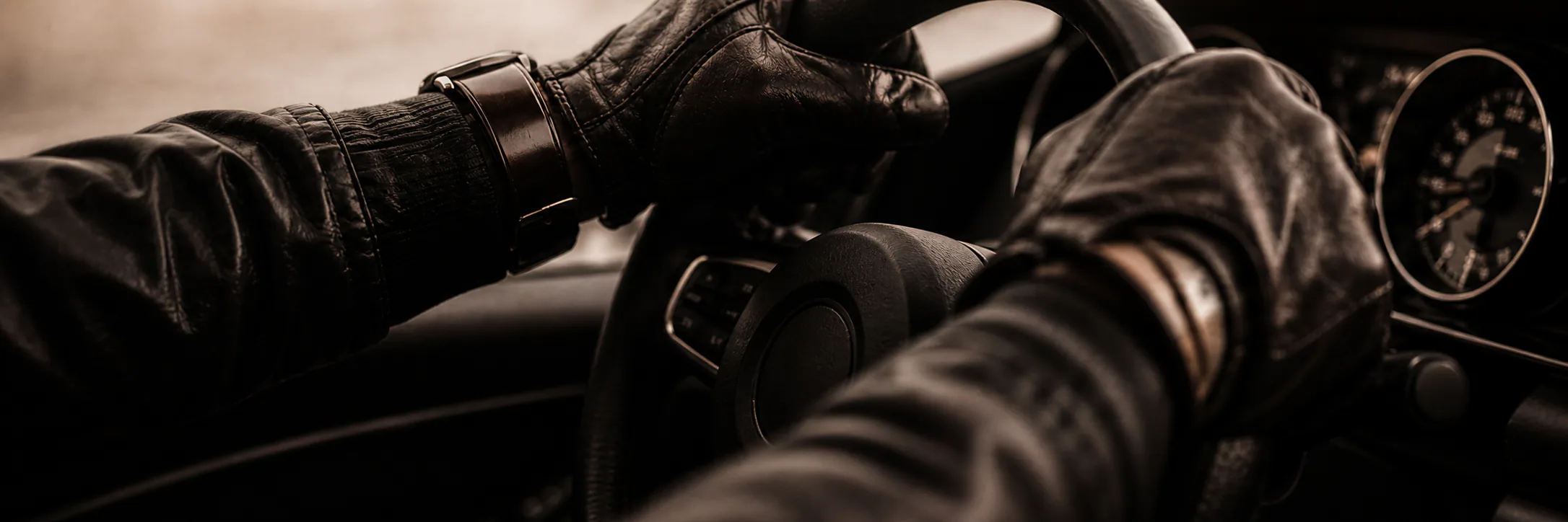 Leather-gloved hands guiding a grand touring car through a bend