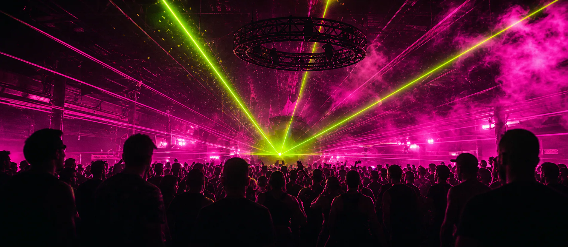 A crowd watching green lasers cut through a magenta room