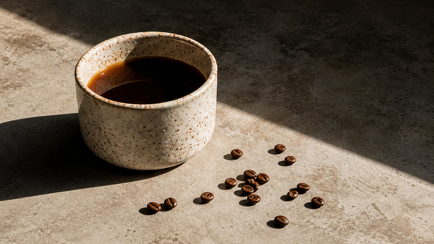 A handmade ceramic cup of black coffee with roasted beans