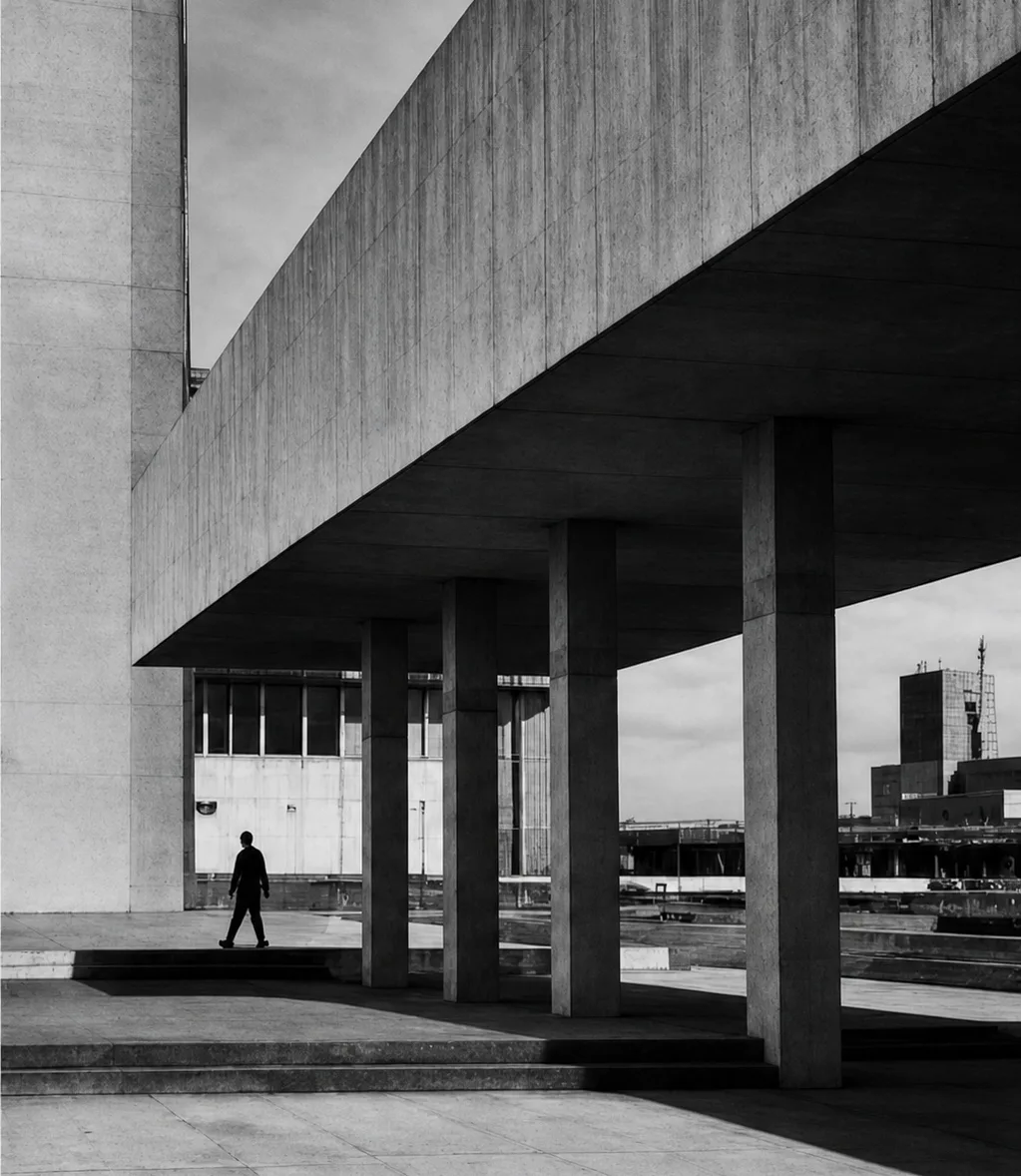 A person walking beneath the concrete canopy of a civic building